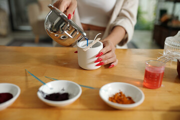 Close-up of woman making candles from soy wax, she pouring it in the form