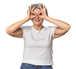 Caucasian mid-age female on studio background showing okay sign over eyes