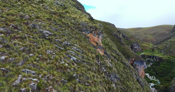 Beautiful drone shot of a group of mountains with vegetation and rock formations forming caves around them next to Millpu Lake in Ayacucho, Peru.