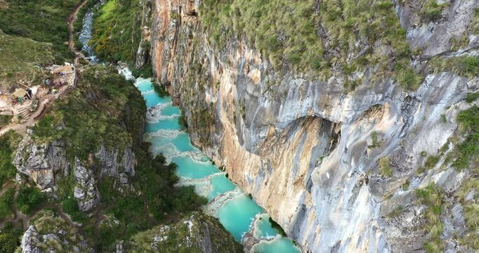 Amazing aerial drone shot gently approaching a lake with turquoise water called Millpu located in Ayacucho in Peru on a hot afternoon. The drone approaches the door of a cave in the mountains.