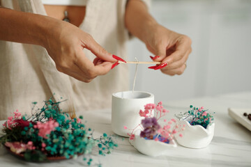 Close-up of woman putting wick in handmade candle and decorating it with dried flowers