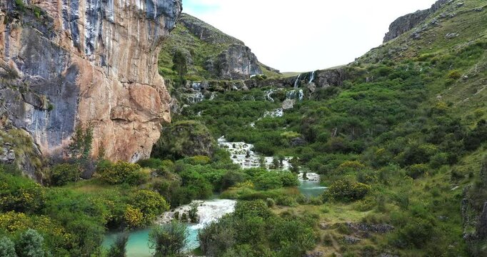 Beautiful drone shot across a lake with turquoise waters in Ayacucho, Peru called Millpu in the middle of mountains with vegetation during a late afternoon.