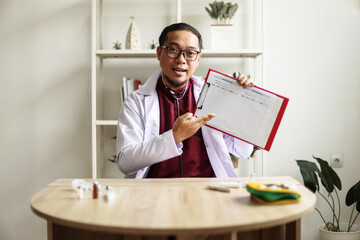 Asian Man Doctor Talking Online With Patient Using Laptop And Showing Blood Sugar Log