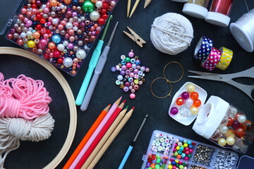 Fototapeta premium Colorful beads, coloring pencils, glitter, needles, string, hoop, tape and scissors on dark background. Various colorful craft supplies. Flat lay.