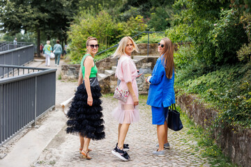 Back view three cheerful young adult women friend walk street old european german town city street park enjoy have fun laughing sunny day together. Female persons friendship celebration party weekend