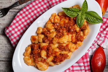 Tasty plate of potato gnocchi topped with Bolognese meat sauce and decorated with fresh basil leaves.