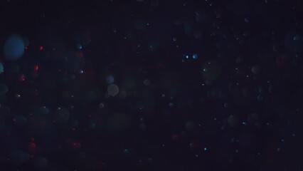 Vibrant red and blue dust particles with bokeh lens blur and glowing trails against a black...