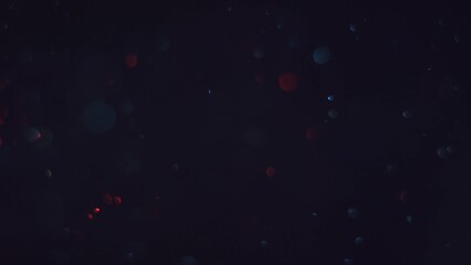 Vibrant red and blue dust particles with bokeh lens blur and glowing trails against a black...