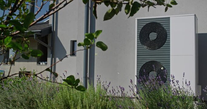 Outdoor heat pump unit with lavender plants in a modern garden setting, with a house in the background.