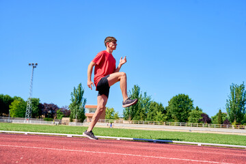 A man in a red shirt and black shorts is running on a track