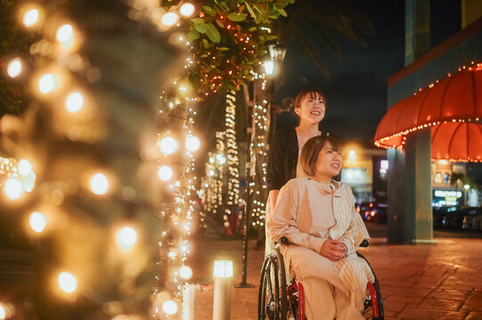 夜に車椅子に乗った日本人女性が友人と夏の沖縄旅行を楽しんでいる