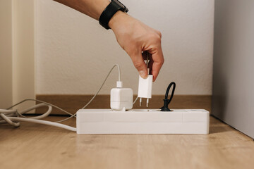Human hand puts the charger into a filled extension cord. White cable connector. Close-up. Home routine