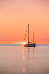 Sailboat Over The Horizon At Sunrise. Moored On Calm Waters, With The Sun Rising On The Horizon, With An Orange Glow In The Sky And Reflections On The Water Of The Mediterranean. Collioure (Cotlliure)