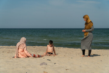 Muslims on the beach, mother with son and daughter, hijab, girls in hijab walking on the beach, Muslims relaxing at sea, travel, Muslims having fun on the beach, boy in bathing shorts