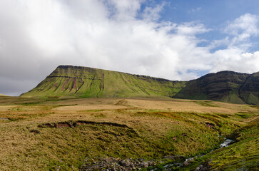 A green mountain range with grassy fields under a partly cloudy sky in Wales.