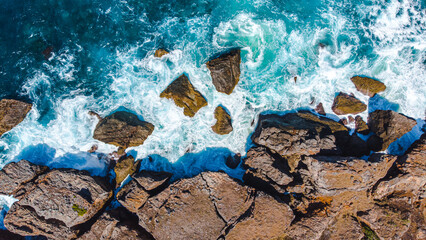 Turquoise waters break violently against the rocky coastline, creating a dynamic seascape