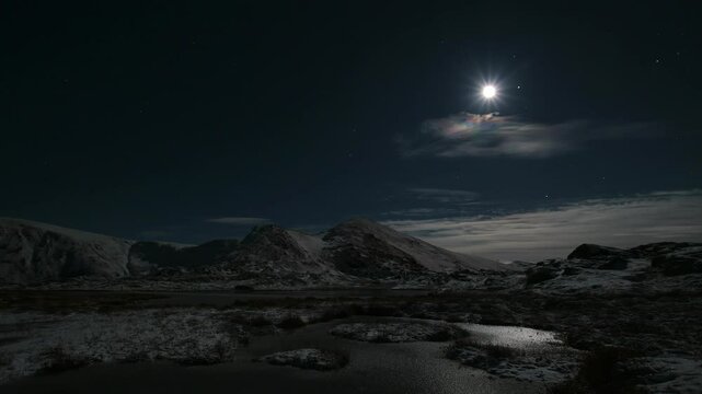 Aurora over mountains with moon and bit of cloud cover.