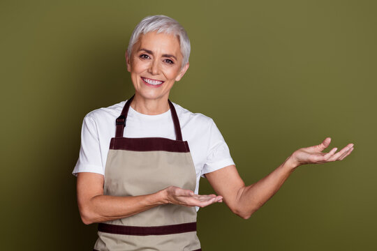 Photo of cheerful pretty lady dressed apron owning cafe showing arms empty space isolated green color background - Powered by Adobe