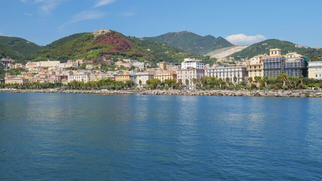 Salerno, Italy. View from the sea of ​​the seafront of the city of Salerno. Buildings in the center, Arechi Castle. Green hills and highway overpass. Crescent building. Real time 4K video.