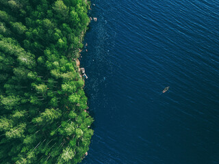 Aerial drone view of blue water lake with fishing boat and green summer woods in Finland.