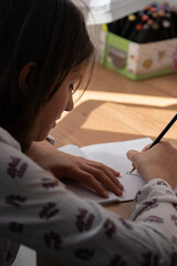 Schoolgirl writes in a notebook on wooden desk in her home.