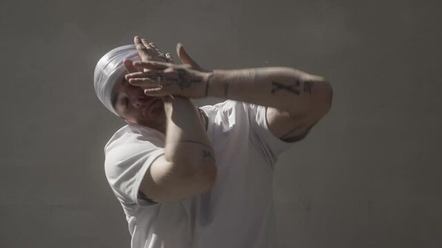 A male dancer with tattoos and a durag performs a fluid and dynamic freestyle dance. His expressive gestures and smooth moves showcase flexibility, confidence, and self-expression in an urban style.