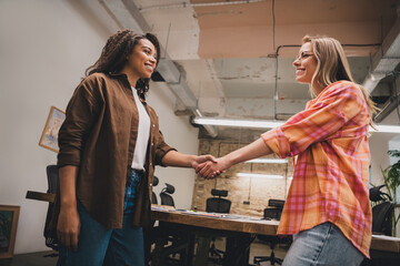 Portrait of two young corporate girls shake hands coworking loft interior business center office...