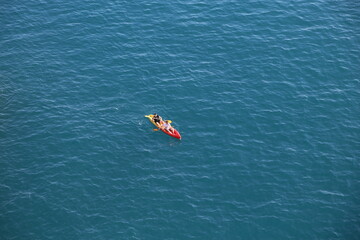Fototapeta premium blue sea water, red yellow boat with oars floats, two people sport Dubrovnik, Croatia April 22, 2023
