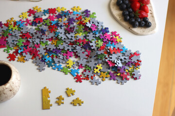 Colorful jigsaw puzzle pieces, cup of tea or coffee, eyeglasses and fresh berries for snacking. Hygge at home. Selective focus.