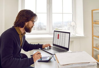 Man sitting at an office desk, working on a laptop computer and using a calculator. Busy financial...