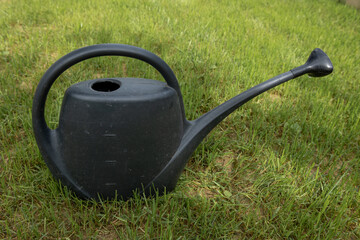 Garden black watering can placed on green lawn.