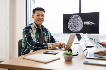 Smiling IT expert working on developments of artificial intelligence in modern office setting. Engaged in technology and innovation. Collaborative work environment focusing on advanced AI projects.