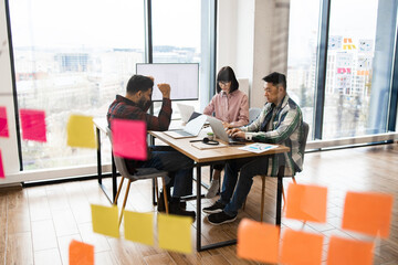 Group of architects collaborating in modern office, discussing project ideas. Team working around table with laptops and documents, brainstorming concepts, and making plans.