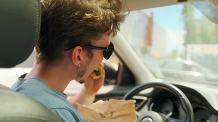 Rear view young guy bites burger removing hunger sitting in car on city street, close up. Slow motion.