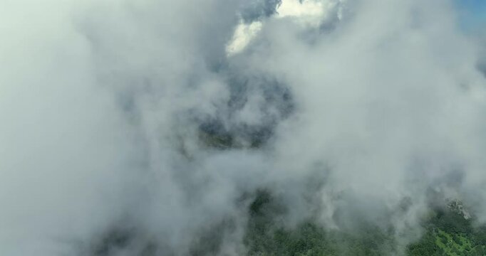 Flying trough white fluffy clouds above green mountain peaks. Beautiful summer sunny day on the high altitude with thick clouds and scenic landscape in background. Cinematic nature aerial video in 4K