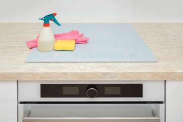 Spray bottle, pink rubber protective gloves and foam sponge on light gray induction stove top....