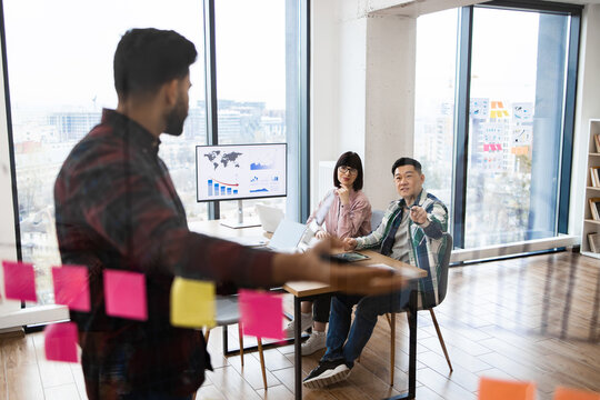 Group of colleagues conducting brainstorming session in modern office using sticky notes and digital charts. Team members discussing ideas, collaborating on project planning and strategies.
