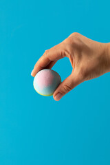 Woman holds colourful bath bomb carefully on blue background