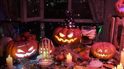 Halloween background with cool pumpkin Jack lantern holding beer mug in creepy hands among flickering candle, mist and festive party lights.