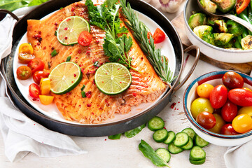 Grilled salmon and vegetables on wooden light background. Dinner table with cooked fish, tomatoes, asparagus