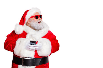 Portrait of cheerful santa claus in hat looking dreamy  using cell phone plan newyear party wearing belt eyewear eyeglasses isolated over red background