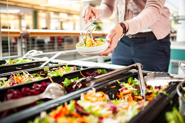 Frische Salate in einem Salatbuffet, eine Frau bedient sich am Buffet