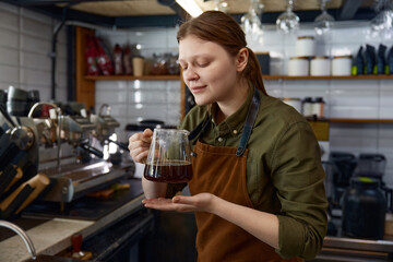 Glad woman barista inhales aroma of freshly prepared coffee