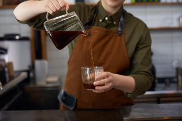 Cropped shot of woman barista pouring transparent brown aroma coffee drink
