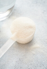 Collagen powder in a plastic measuring spoon and a glass of water in the background