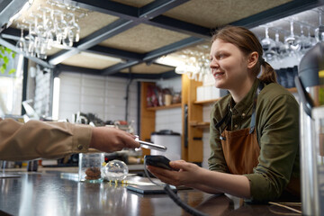 Client paying for coffee order at counter desk with barista holding pos terminal
