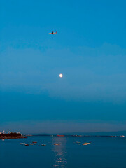 The plane flies over the sea and the moon in the sky