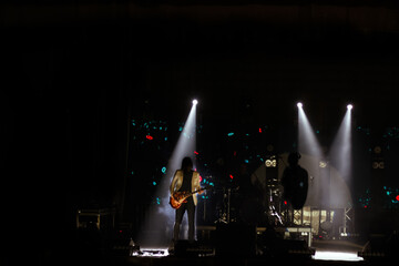 Obraz premium stage at night during a concert, with a band performing. The silhouette of a guitarist is illuminated by stage lights, creating a striking contrast against the dark background