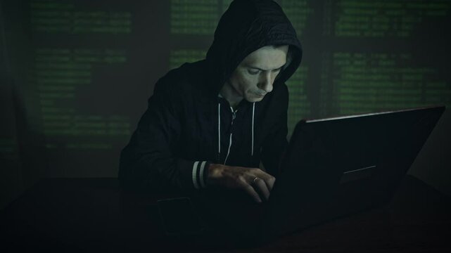 Male hacker in the hood holding the phone in his hands trying to hack the mobile device cloud and steal data in neon light. The concept of cyber security