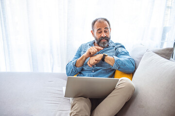 Mature Man Checking Time While Working on Laptop at Home